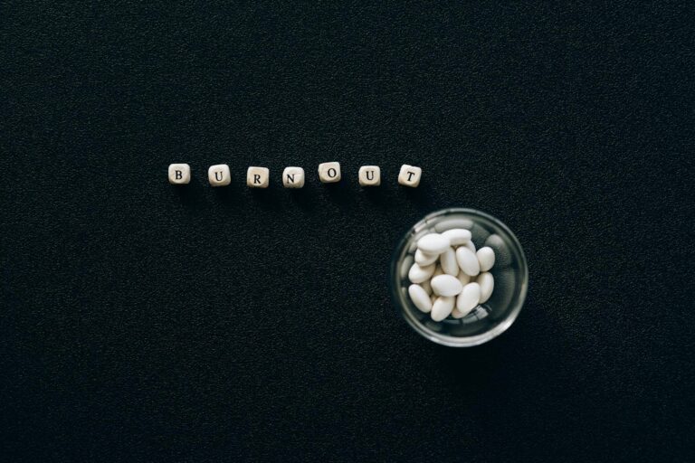 A conceptual image depicting burnout using pills and scrabble tiles on a black surface.