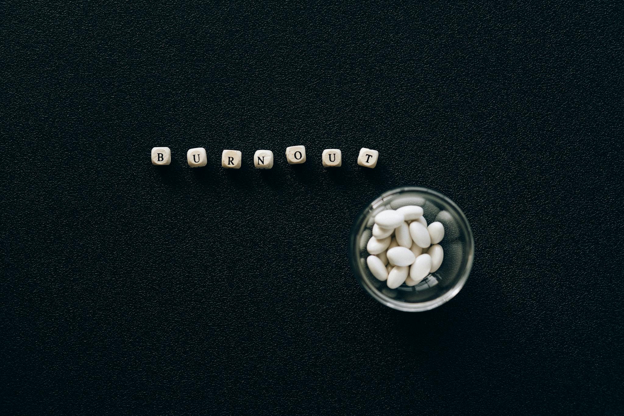 A conceptual image depicting burnout using pills and scrabble tiles on a black surface.